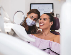 patient looking into a dental mirror to see her teeth with the dentists