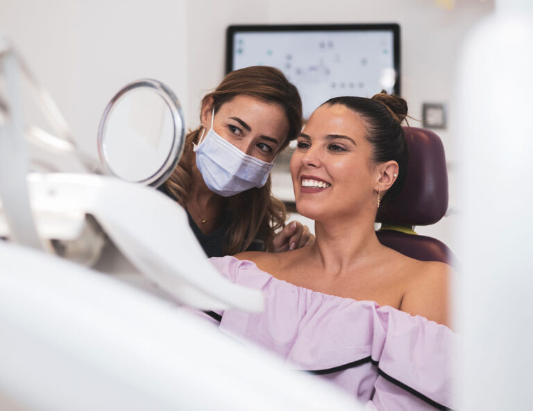 patient looking into a dental mirror to see her teeth with the dentists