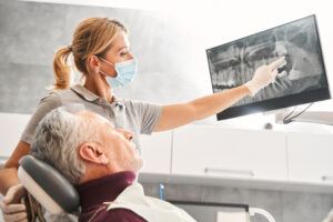 A dentist is carefully explaining the process for dental implants to a patient, using a model of a jaw with implants to illustrate each step. No text on image.