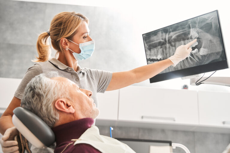 A dentist is carefully explaining the process for dental implants to a patient, using a model of a jaw with implants to illustrate each step. No text on image.